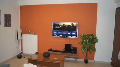 a living room with an orange wall with a flat screen tv at Electra in Saronida