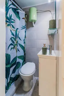 a bathroom with a toilet and a green leafy shower curtain at Green boho apartment in Athens