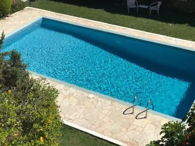 a swimming pool with blue water and rocks in a yard at Grand Villa Lagonisi in Kalívia Thorikoú