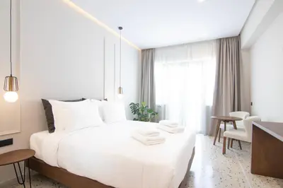 a white bedroom with a large bed and a table at Mythodea Athens Suites in Athens