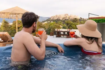 a man and woman sitting in a swimming pool with drinks at Visum Acropol ,3BR - Private Terrace-Jacuzzi - Amazing View in Athens