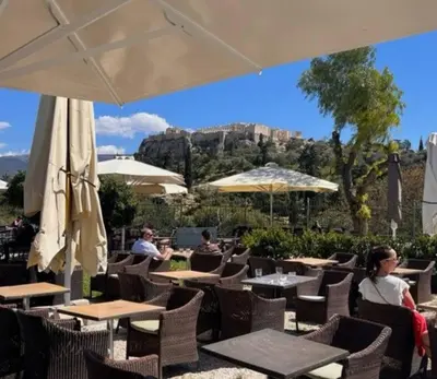 a group of people sitting at a restaurant with tables and umbrellas at James - 2BR in the Heart of Ancient Athens in Athens