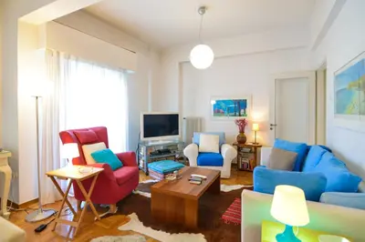 a living room with blue and red chairs and a tv at Athens Stylish apt next to the beach and port in Athens