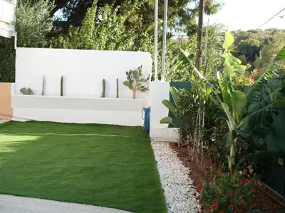 a garden with green grass and a white wall at ILIADA Luxury Apartment in Porto Rafti