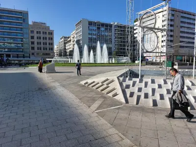 a man walking past a fountain in a city at Retro Stay Athens in Athens
