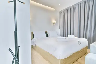 a white bedroom with a white bed and a chair at Glassy Apartment in Athens