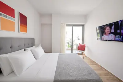 a white bedroom with a bed and a tv on the wall at Costa Alimos by Verde Apartments in Athens