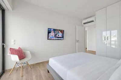 a white bedroom with a white bed and a chair at Costa Alimos by Verde Apartments in Athens