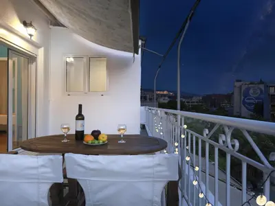 a table with two glasses of wine and fruit on a balcony at Acropolis View top floor apartment in Athens