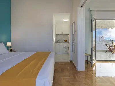 a white bedroom with a large bed and a kitchen at Acropolis View top floor apartment in Athens