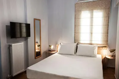 a bedroom with a bed with white sheets and a window at Pagrati Hilton location Bentzi Family Suite 5 in Athens