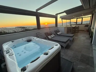 a bath tub on a balcony with a sunset in the background at Alex Suite Θερμαινόμενο Τζακούζι & Θέα Ακρόπολη in Athens