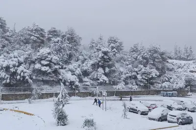 two people walking in a snow covered parking lot with cars at Agnes apartment Filopappou in Athens