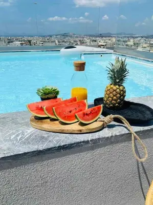 a plate of watermelon and a pineapple on a table by a pool at New 2BD aprt with Shared Rooftop Pool D3 in Athens