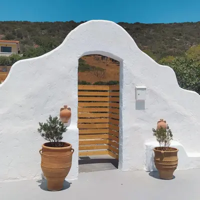 a white building with a door and two potted plants at BY THE SEA ROOMS, AVLAKI in Porto Rafti