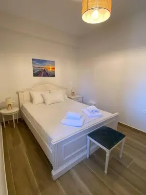 a bedroom with a white bed with a blue stool at Sea Through Apartment Anavissos in Anavissos