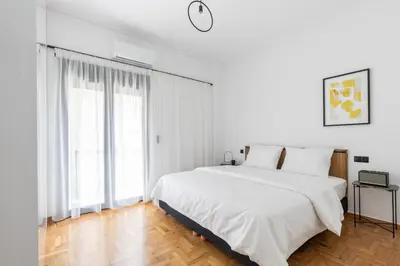 a white bedroom with a bed and a large window at Elliot Neapoli, Athens in Athens