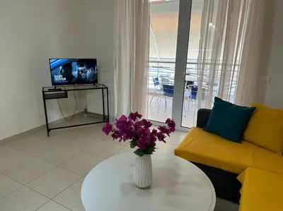 a living room with a yellow couch and a vase with purple flowers at Riviera beach, seaside spacious apt. in Anavissos