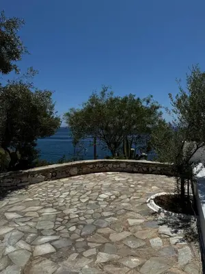 a stone patio with trees and water in the background at Attica Vacation Home in Dhaskalión