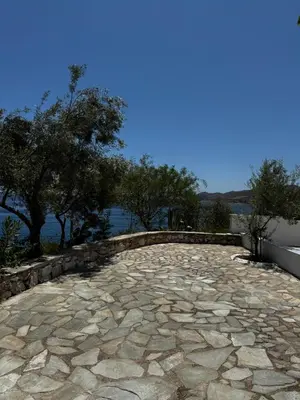 a stone patio with trees and water in the background at Attica Vacation Home in Dhaskalión