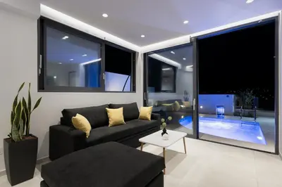 a living room with a black couch and large windows at White Cliff Luxury Suites in Porto Rafti