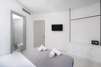 a white bedroom with a bed and a bathroom at White Cliff Luxury Suites in Porto Rafti