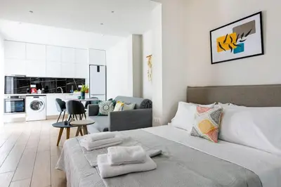 a white bedroom with a large bed and a kitchen at The Charm Studio in Glyfada in Athens