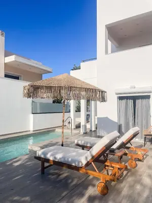 a group of lounge chairs and an umbrella next to a swimming pool at My Porto Villa in Porto Rafti