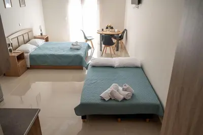 a room with two beds and a table with a chair at Anesis Airport rooms 204 in Koropíon