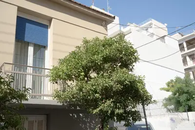 a white building with a tree in front of it at Casanova94 Guesthouse in Piraeus