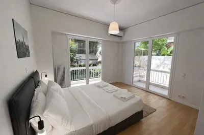 a bedroom with a bed with white sheets and windows at Modern flat close to the beach-ground floor in Athens
