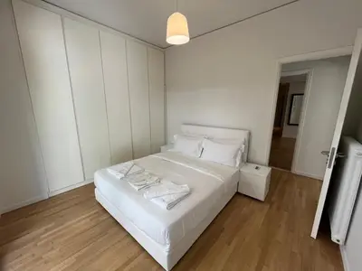 a white bedroom with a large white bed and wooden floors at Modern flat close to the beach-ground floor in Athens