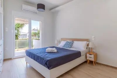 a white bedroom with a bed and a window at Cozy 2BD Beachfront Escape In The Heart Of Glyfada in Athens