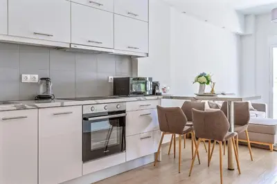 a kitchen with white cabinets and a table with chairs at Cozy 2BD Beachfront Escape In The Heart Of Glyfada in Athens