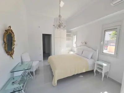 a white bedroom with a bed and a table and a mirror at NN Rooms and Suites near Athens Airport in Spáta