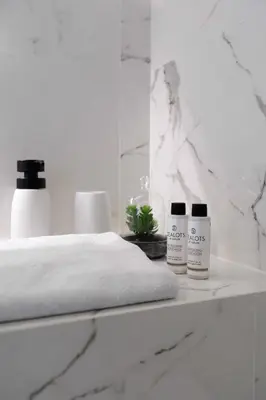 a white bedroom with a bed and two products on a shelf at Sunshine Suite by Athens Riviera Suites in Saronida