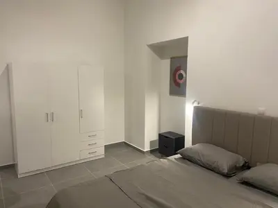 a white bedroom with a bed and a cabinet at Leo's Apartments in Koropíon