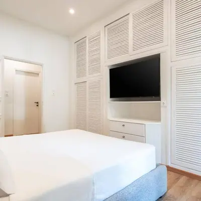 a white bedroom with a bed and a flat screen tv at 4BD Apartment with Outdoor Jacuzzi Garden in Athens