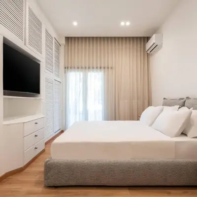 a white bedroom with a large bed and a flat screen tv at 4BD Apartment with Outdoor Jacuzzi Garden in Athens