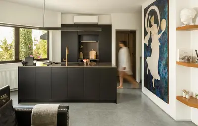 a woman walks through a kitchen with a black island at Sol Residence - Private Pool Gym Glyfada in Athens