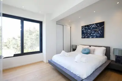 a white bedroom with a large bed with a blue pillow at Ellinikon Luxury Apartment in Athens