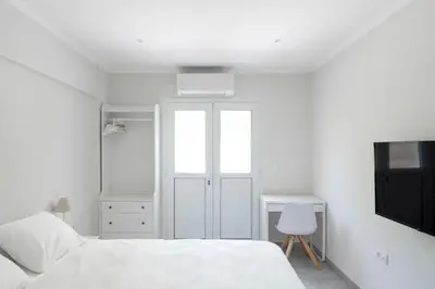 a white bedroom with a bed and a tv at Voula's Secret Garden Studio in Athens