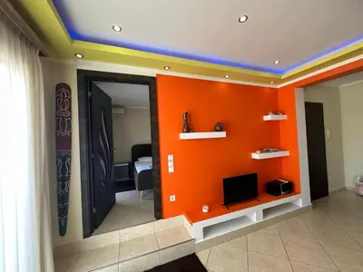 a room with an orange wall with a tv on a shelf at Riviera Beach apart no 5 in Anavissos