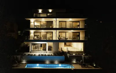 a tall building with a pool in front of it at night at Experience Penthouse by Athens Riviera Suites in Saronida