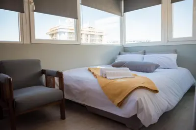 a bedroom with a bed and a chair and windows at 3C’s Athens South @Delta: SNFCC / Faliro Seaview Penthouse in Athens
