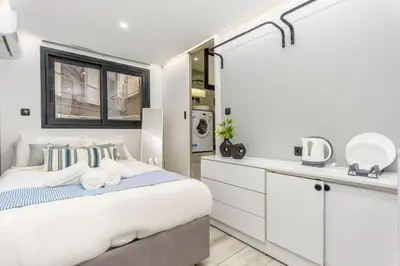 a white bedroom with a bed and a kitchen at The Oh Boy Studio in Athens in Athens