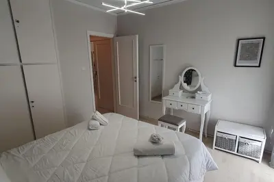a white bedroom with a bed and a mirror at Seaside Beauty 5 min Vouliagmeni Beach in Athens