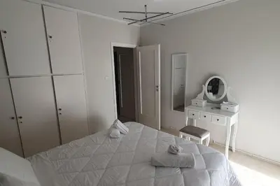 a white bedroom with a large bed and a mirror at Seaside Beauty 5 min Vouliagmeni Beach in Athens