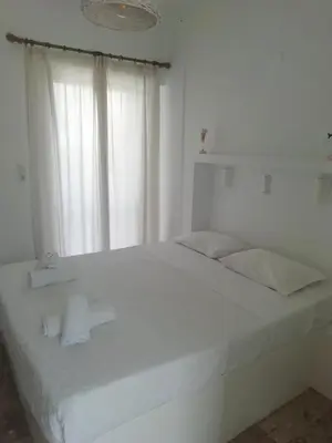a white bed in a white room with a window at Golden Star Praxitelous in Agia Marina Aegina