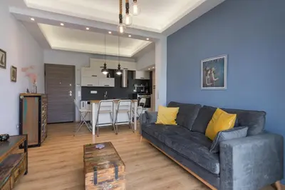 a living room with a gray couch and a kitchen at Stratum Apartment by LobbySquare in Athens
